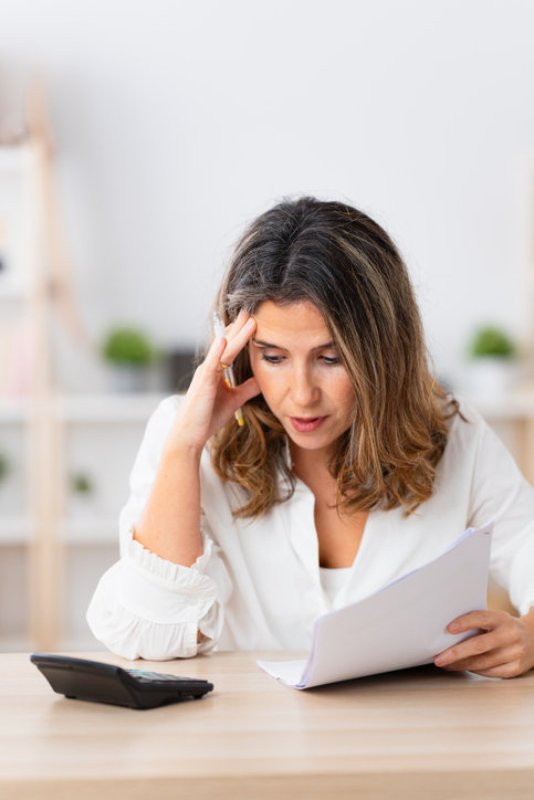 Worried woman about domestic finances using calculator at home